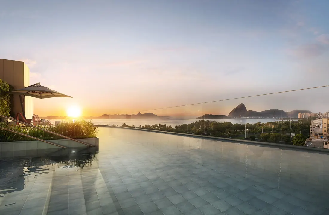 Piscina com raia e borda infinita do Glória Residencial ao pôr do sol, com o Pão de Açúcar ao fundo